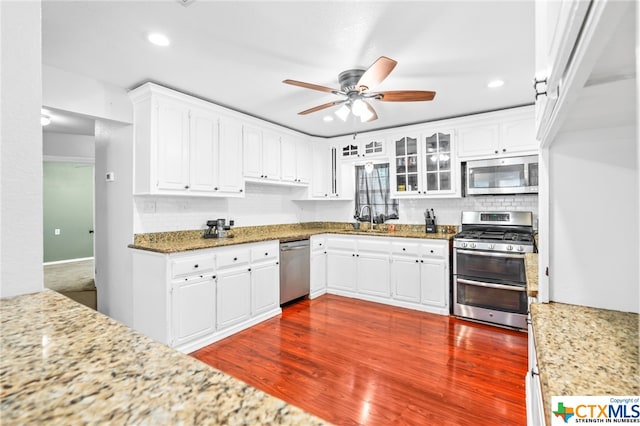 kitchen with light stone countertops, stainless steel appliances, sink, white cabinets, and dark hardwood / wood-style floors