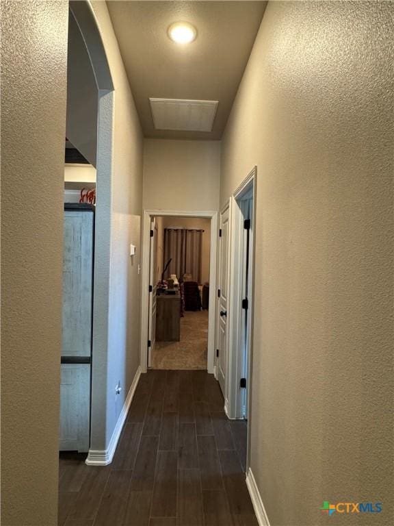 corridor with wood tiled floor, a textured wall, arched walkways, and baseboards