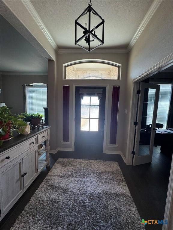 foyer featuring dark wood-style flooring, a notable chandelier, crown molding, and baseboards