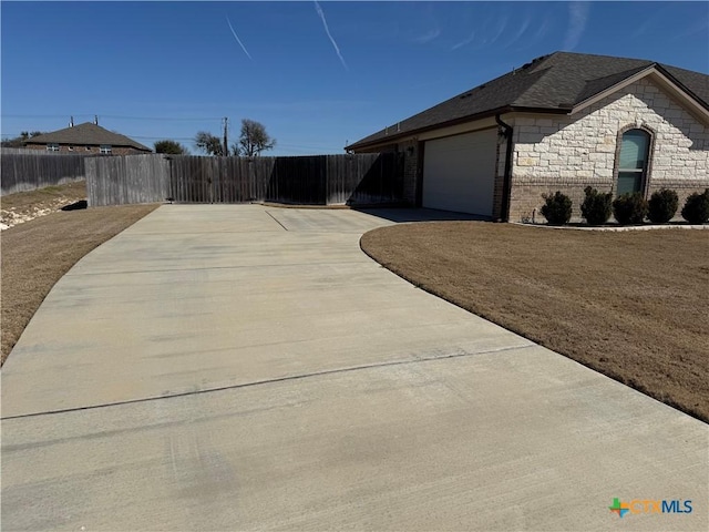 view of home's exterior featuring brick siding, fence, a garage, stone siding, and driveway