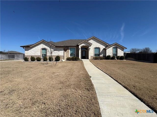 french country home featuring stone siding, fence, and a front lawn