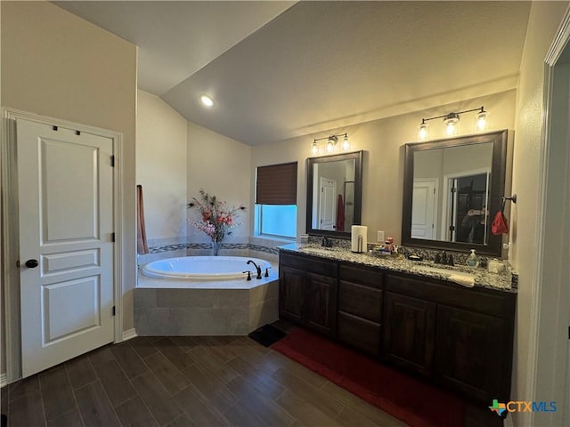 full bathroom with double vanity, wood finished floors, a garden tub, vaulted ceiling, and a sink