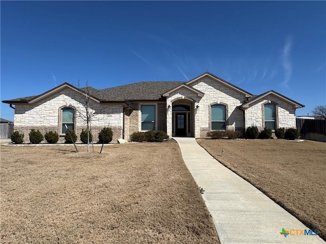 french provincial home featuring brick siding, roof with shingles, and fence