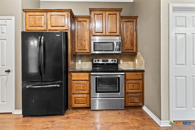 kitchen with stainless steel appliances, wood-type flooring, dark stone countertops, and decorative backsplash