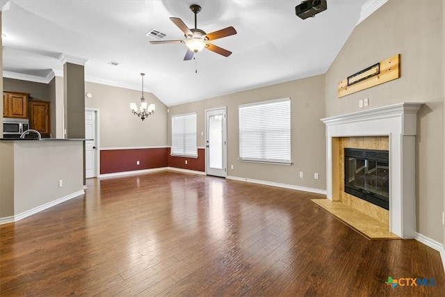 unfurnished living room with ceiling fan with notable chandelier, lofted ceiling, dark wood-type flooring, a tile fireplace, and ornamental molding