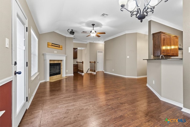 unfurnished living room featuring dark hardwood / wood-style flooring, a tiled fireplace, ornamental molding, and ceiling fan with notable chandelier