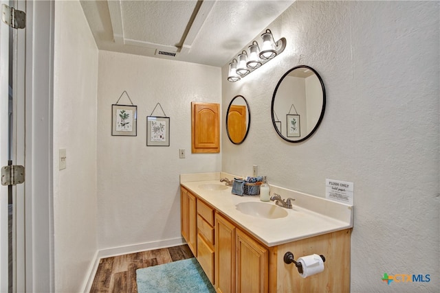 bathroom with a textured ceiling, wood finished floors, a sink, and visible vents