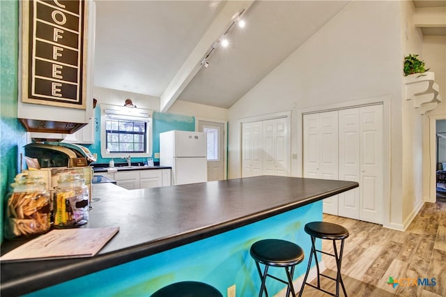 kitchen with dark countertops, lofted ceiling with beams, a breakfast bar, freestanding refrigerator, and light wood-style floors