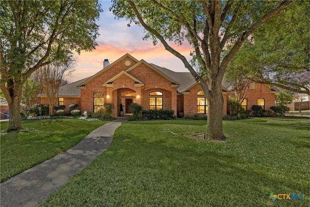 view of front of property featuring brick siding, a front lawn, and a chimney