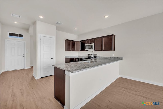 kitchen featuring light stone counters, dark brown cabinets, light hardwood / wood-style flooring, kitchen peninsula, and stainless steel appliances