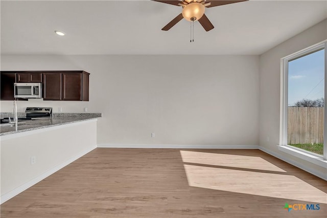 kitchen featuring dark brown cabinets, light hardwood / wood-style flooring, appliances with stainless steel finishes, ceiling fan, and light stone countertops