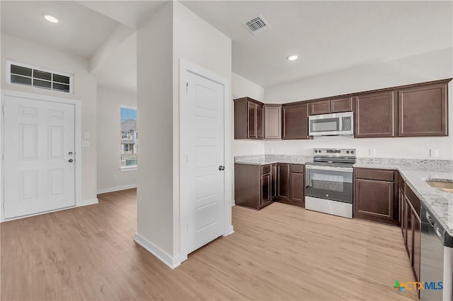 kitchen featuring stainless steel appliances, light stone countertops, dark brown cabinetry, and light wood-type flooring