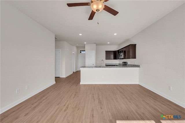 kitchen featuring sink, light hardwood / wood-style flooring, dark brown cabinets, light stone countertops, and kitchen peninsula