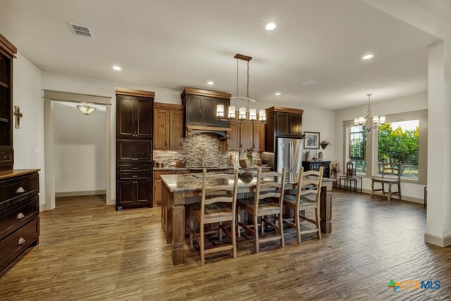 kitchen featuring a breakfast bar, light stone counters, a chandelier, stainless steel fridge, and an island with sink