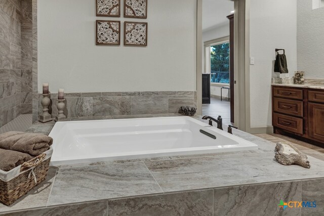 bathroom with vanity and tiled bath