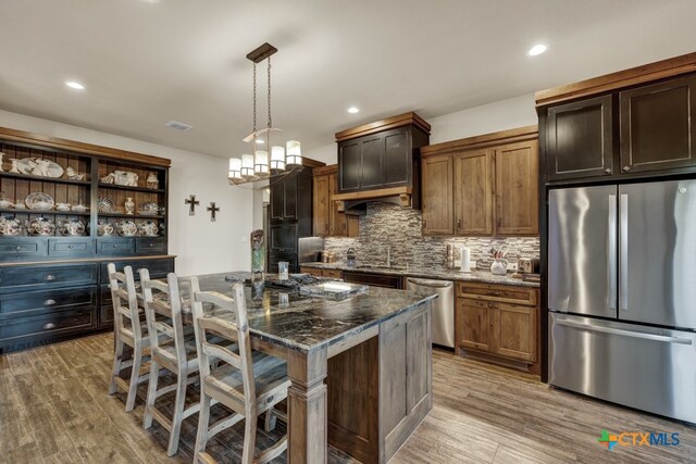 kitchen with a breakfast bar, dark stone counters, an island with sink, pendant lighting, and stainless steel appliances