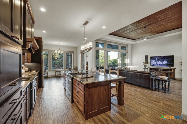 kitchen with pendant lighting, a kitchen breakfast bar, dark stone counters, a kitchen island with sink, and gas stove