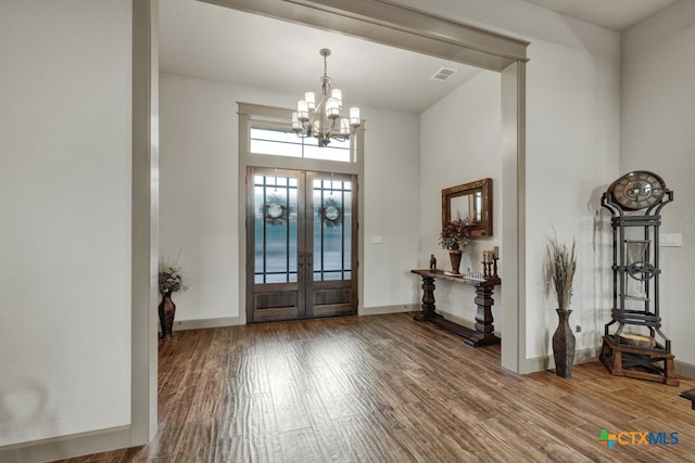 entrance foyer featuring french doors, a towering ceiling, an inviting chandelier, and hardwood / wood-style floors