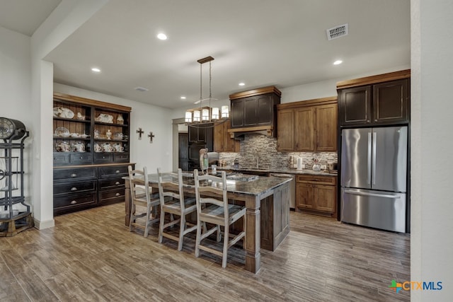 kitchen featuring a breakfast bar, dark stone counters, pendant lighting, stainless steel appliances, and a kitchen island with sink