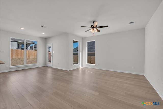 empty room featuring ceiling fan, light wood finished floors, visible vents, and baseboards