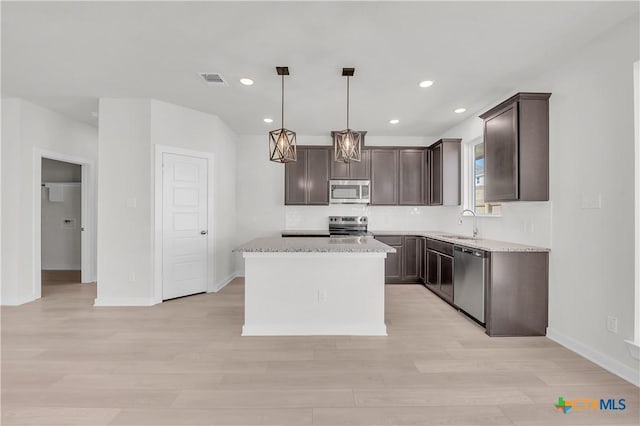 kitchen featuring a center island, hanging light fixtures, stainless steel appliances, light wood-type flooring, and a sink