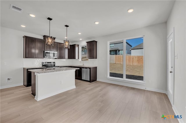 kitchen featuring a kitchen island, visible vents, light wood-style floors, appliances with stainless steel finishes, and decorative light fixtures