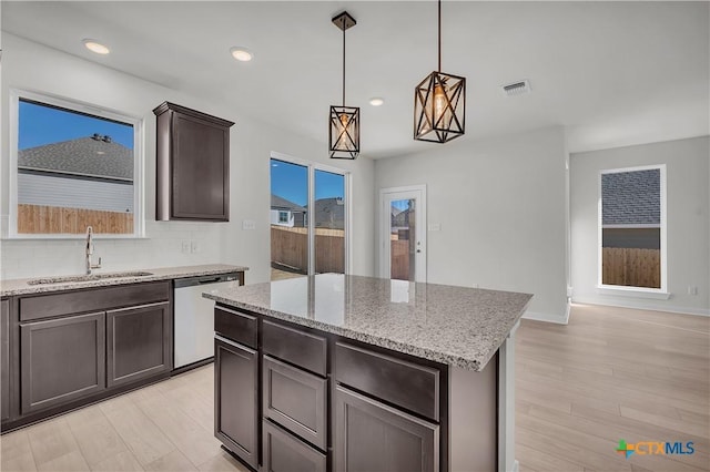 kitchen with visible vents, dishwasher, a kitchen island, hanging light fixtures, and a sink