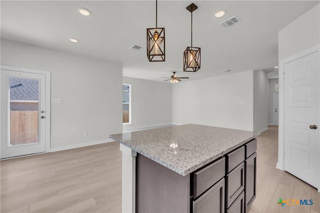 kitchen featuring light wood-type flooring, visible vents, hanging light fixtures, and light stone countertops