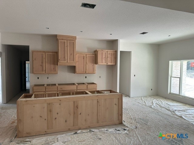 kitchen with light brown cabinets, a textured ceiling, and a kitchen island