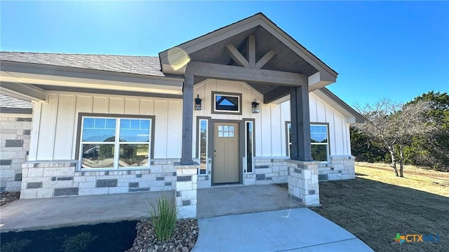 doorway to property with stone siding, board and batten siding, and roof with shingles