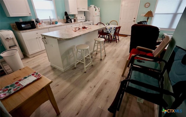 kitchen featuring white cabinets, light wood-type flooring, white appliances, and a kitchen island