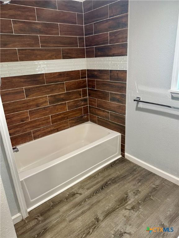 bathroom featuring baseboards,  shower combination, and wood finished floors