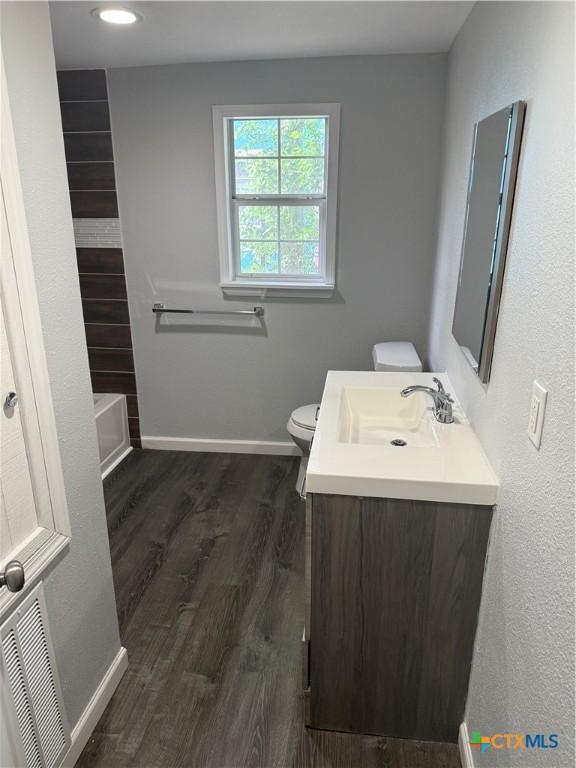full bathroom with vanity, toilet, a tub, baseboards, and wood finished floors