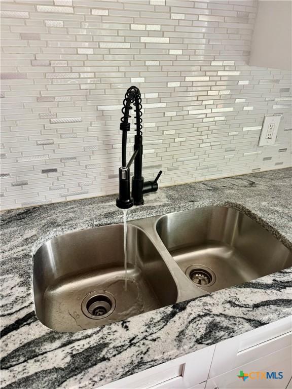 interior details featuring a sink, tasteful backsplash, and light stone countertops