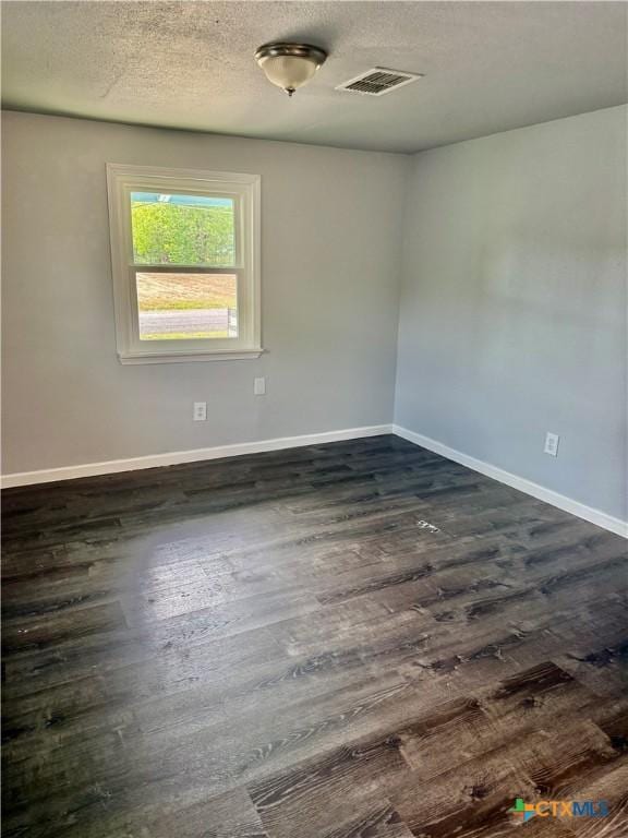 empty room featuring visible vents, a textured ceiling, baseboards, and dark wood-style floors