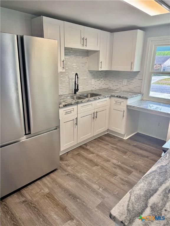 kitchen featuring freestanding refrigerator, white cabinetry, light stone counters, a sink, and light wood-style flooring