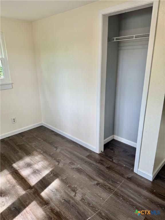 unfurnished bedroom with a closet, baseboards, and dark wood-type flooring