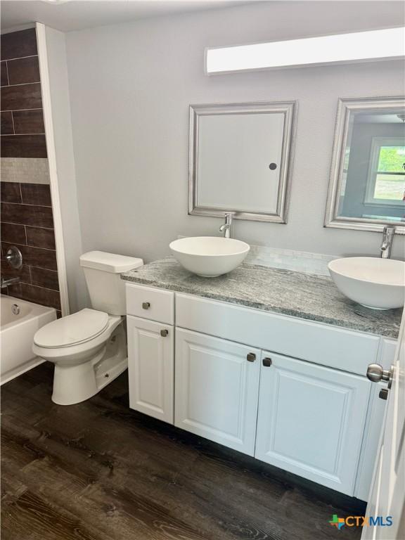 bathroom featuring a sink, double vanity, toilet, and wood finished floors