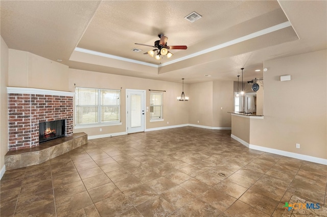 unfurnished living room featuring tile patterned flooring, a tray ceiling, a fireplace, a textured ceiling, and ceiling fan with notable chandelier