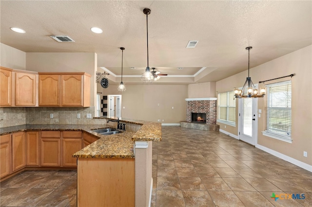 kitchen with stone countertops, decorative light fixtures, sink, decorative backsplash, and kitchen peninsula