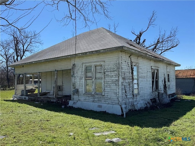 view of side of property featuring a porch, a lawn, and roof with shingles