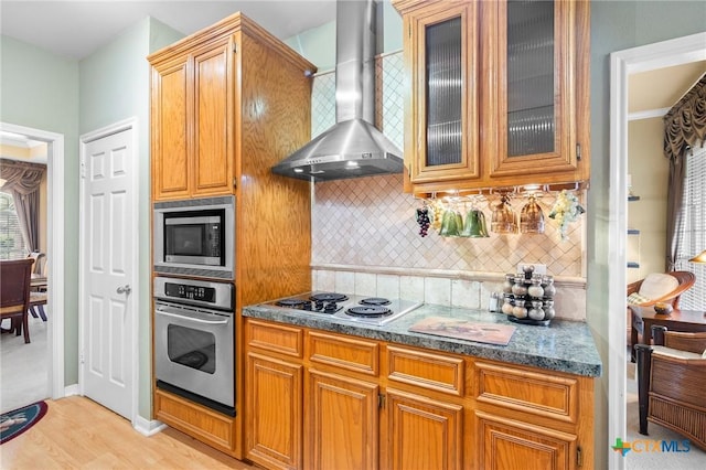 kitchen featuring light wood-style floors, backsplash, appliances with stainless steel finishes, and wall chimney range hood
