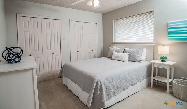 bedroom featuring multiple closets, ceiling fan, light colored carpet, and a textured ceiling