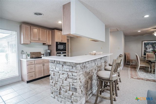 kitchen with a textured ceiling, black microwave, light brown cabinets, a kitchen breakfast bar, and kitchen peninsula