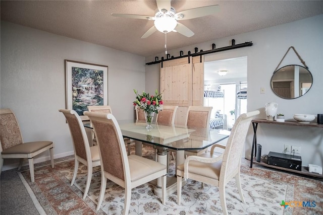 dining room with ceiling fan, a barn door, and a textured ceiling