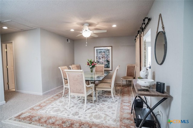 dining area featuring ceiling fan, a barn door, carpet floors, and a textured ceiling