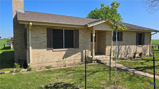 view of front of home featuring brick siding, a chimney, a front lawn, and roof with shingles