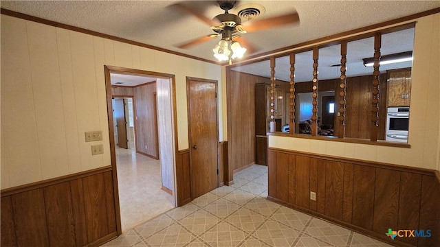 hallway featuring a textured ceiling, crown molding, wood walls, visible vents, and light floors