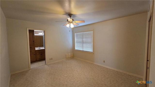 unfurnished bedroom featuring ensuite bathroom, light colored carpet, baseboards, and ceiling fan