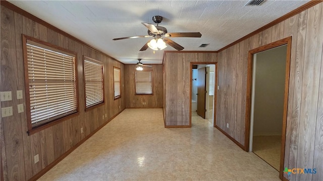 spare room with visible vents, baseboards, ornamental molding, ceiling fan, and wooden walls